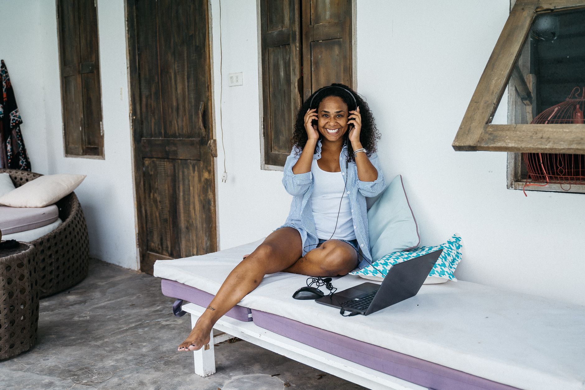 A cheerful woman sitting on a bench outdoors, using headphones and a laptop, enjoying relaxation.